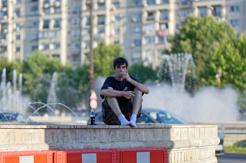 9 - A person sitting casually on the edge of a marble basin near a water fountain in Piata Unirii, a major public square in central Bucharest